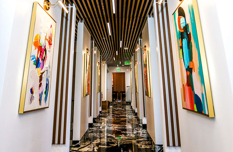 The image depicts an interior corridor with artwork hanging on the walls, illuminated by linear lighting fixtures.