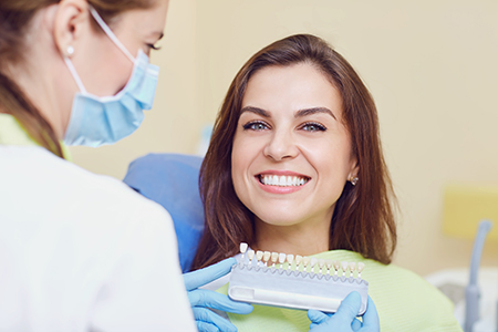 A woman sitting in a dental chair with a dentist inspecting her teeth using a dental mirror.