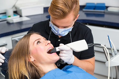 The image shows a dental hygienist performing a teeth cleaning procedure on a patient in a dental office setting.