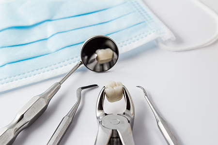 The image displays a collection of dental instruments including a toothbrush with toothpaste on it placed next to dental tools such as tweezers, forceps, and scissors, all set against a blue cloth background.