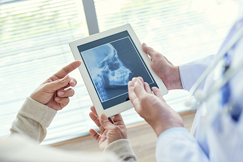The image shows two people examining a medical tablet with an X-ray displayed on it.
