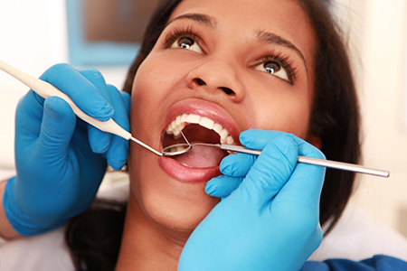 A woman receiving dental care with a hygienist performing an oral examination using a mirror.