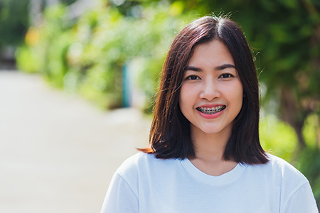 A young woman with short hair wearing a white t-shirt poses for a portrait against a blurred background.