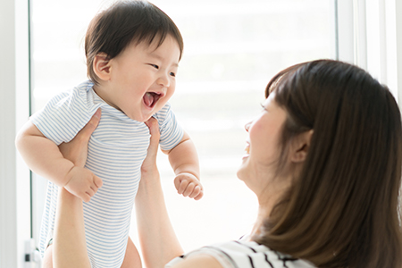 A young woman holding a baby with a joyful expression while smiling at the camera.