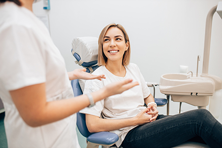 Woman sitting in dental chair with a smile, surrounded by dental professionals who appear to be assisting her.