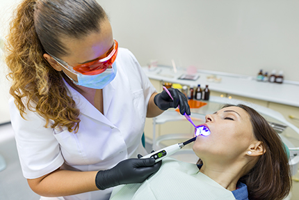 A dental hygienist using a water jet device on a patient s teeth during a cleaning procedure.